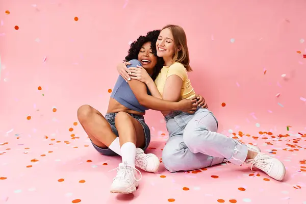 Two diverse women in casual attire relaxing on a pink floor. — Stock Photo