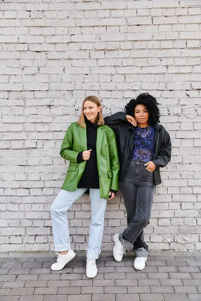 Two attractive diverse women stand near a brick wall. — Stock Photo