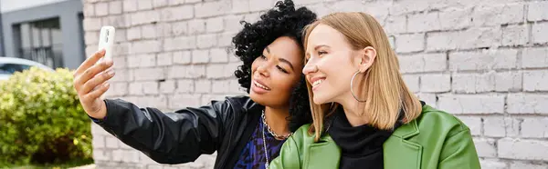 Two attractive diverse women in casual attire taking a selfie with a cell phone. — Stock Photo