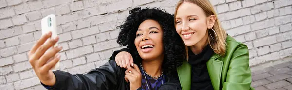 Two diverse women in cozy attire taking a cell phone picture together. — Stock Photo