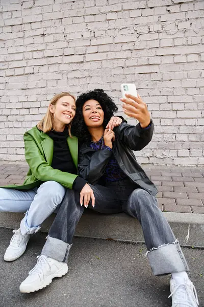 Zwei unterschiedliche Frauen in kuscheliger Kleidung sitzen auf dem Boden und machen ein Foto. — Stockfoto