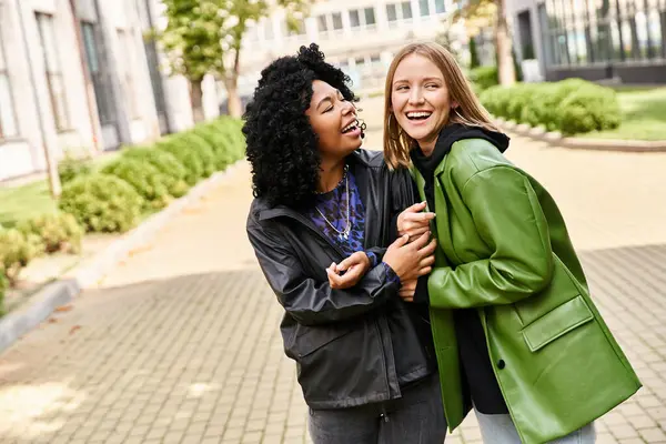 Dos mujeres diversas en traje casual de pie lado a lado en la acera. - foto de stock