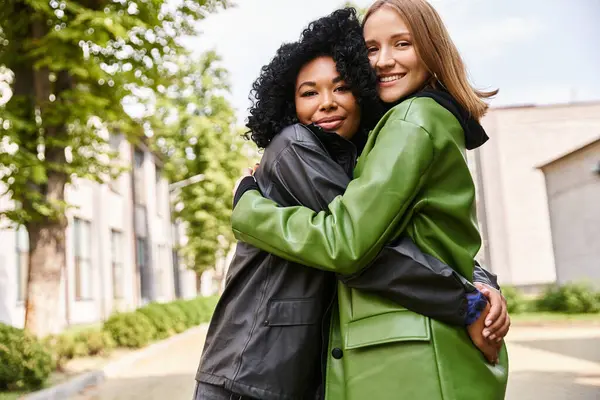 Two diverse women in casual attire share a warm hug in front of a building. — Stock Photo