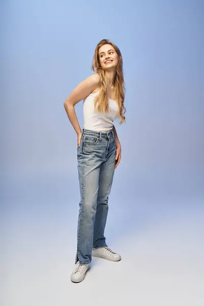 A beautiful blonde woman strikes a pose in a tank top and jeans in a studio setting. — Stock Photo