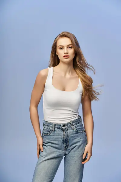 A young, beautiful blonde woman with long hair is casually dressed in jeans and a tank top in a studio setting. — Stock Photo