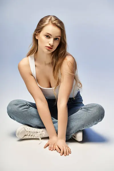 Une superbe jeune femme aux cheveux blonds élégamment assise sur le sol dans un décor de studio. — Photo de stock