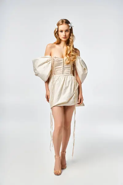 Uma jovem mulher loira fica elegantemente em um vestido branco em um estúdio, exalando graça e charme. — Fotografia de Stock