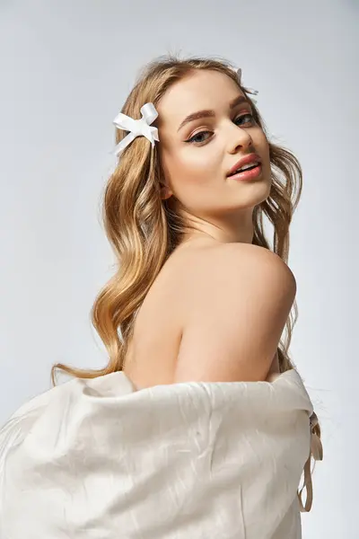 A young, blonde woman exudes elegance with a white bow in her hair in a studio setting. — Stock Photo