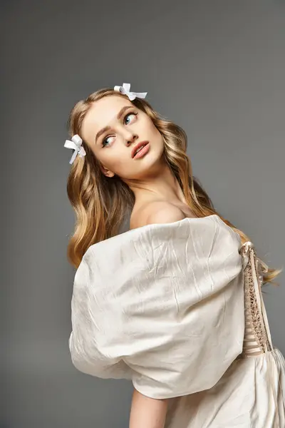 Молодая блондинка источает эфирную красоту в белом платье с нежным цветком, украшающим ее волосы, установленным в студии. — стоковое фото