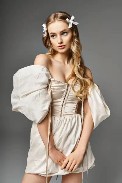 Une jeune femme blonde se tient dans un studio vêtue d'une robe courte et d'un nœud dans les cheveux, respirant un sentiment d'élégance et de douceur. — Photo de stock