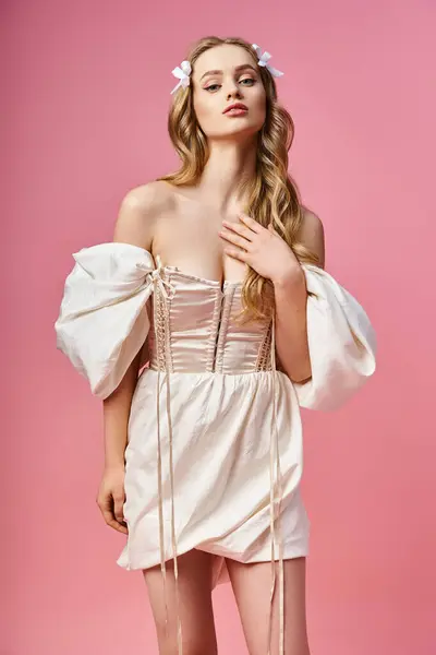 Una joven rubia con un lazo en el pelo posa elegantemente en un vestido blanco que fluye. - foto de stock