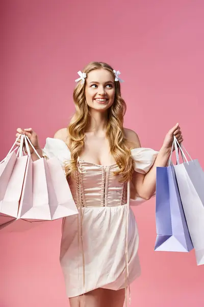 A young, blonde woman in a stylish dress holding shopping bags in a studio setting. — Stock Photo