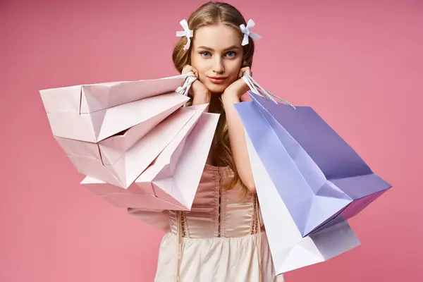 A young blonde woman striking a confident pose while holding shopping bags in a studio setting. — Stock Photo