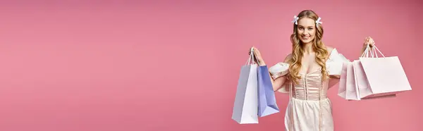 A young, blonde woman in a white dress holding colorful shopping bags against a plain backdrop. — Stock Photo