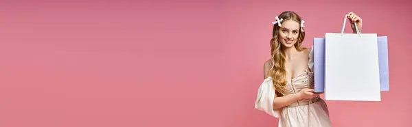 Une jeune femme blonde dans une robe élégante tient gracieusement un sac à provisions dans un cadre de studio. Elle respire l'élégance et l'équilibre. — Photo de stock
