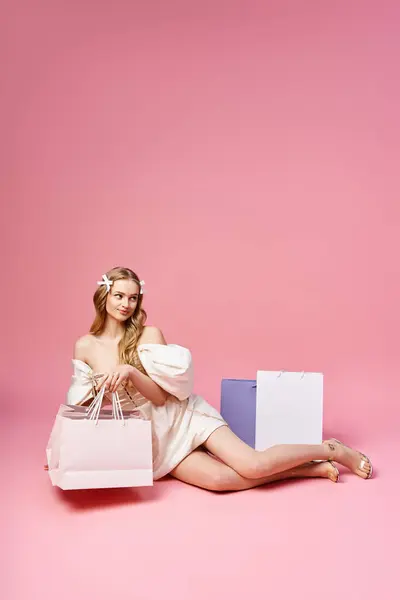 A young blonde woman sits gracefully on the ground, holding a shopping bag, embodying urban chic style. — Stock Photo