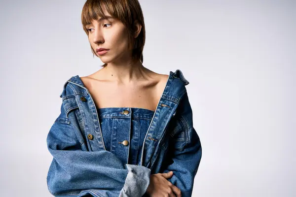 A stylish young woman with short hair strikes a confident pose in a denim jacket in a studio setting. — Stock Photo