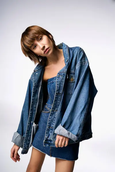 Una mujer joven con el pelo corto posando con confianza en una chaqueta de jean de moda en un entorno de estudio. - foto de stock