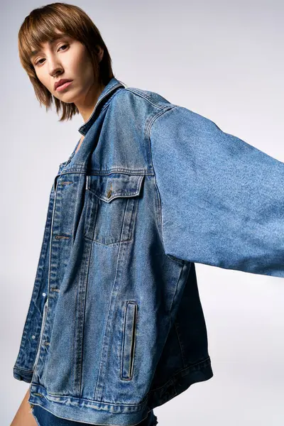 A young woman with short hair is confidently posing for a picture in a studio, wearing a trendy jean jacket. — Stock Photo