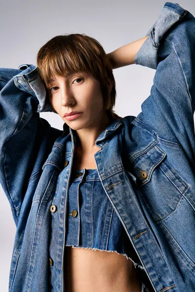 Una mujer joven y elegante con el pelo corto golpeando una pose segura mientras usa una chaqueta de jean en un entorno de estudio. — Stock Photo