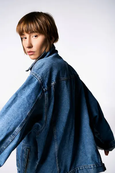 Una giovane donna alla moda che indossa una giacca di jeans posa fiduciosa per la fotocamera in modo trendy e cool. — Foto stock
