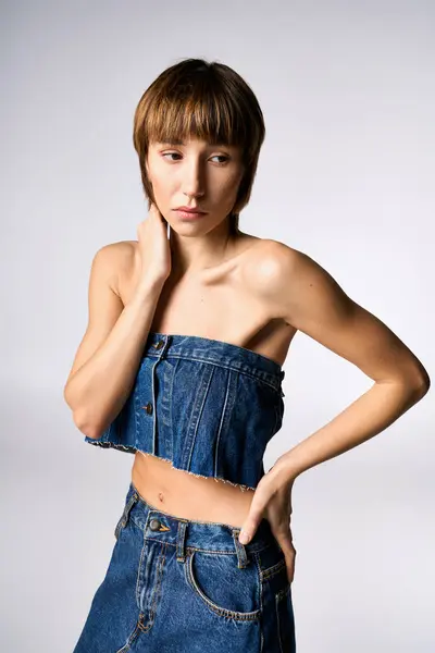 A stylish young woman with short hair posing confidently in a denim dress in a studio environment. — Stock Photo