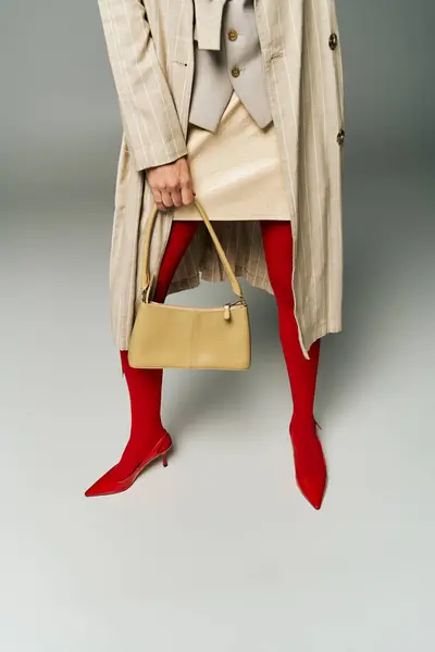 Eine modische junge Frau steht selbstbewusst im Trenchcoat und hält eine stylische Handtasche in der Hand. — Stockfoto