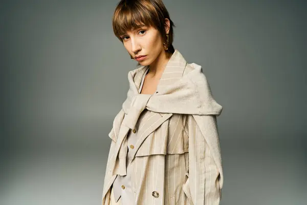 Uma jovem elegante com cabelo curto posa com confiança em um casaco de trincheira para um retrato em um estúdio. — Fotografia de Stock