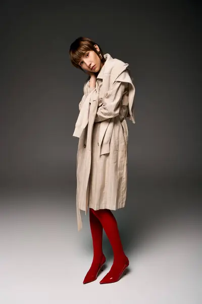 A young woman with short hair standing in a trench coat and red socks in a studio setting. — Stock Photo
