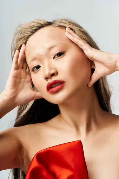 An attractive Asian woman in a vibrant red dress holding her head in a dramatic pose. — Stock Photo