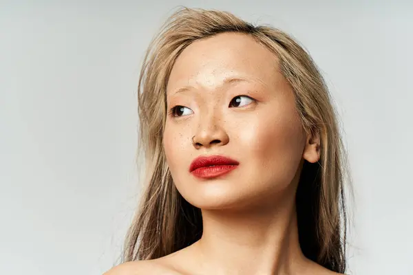 Una atractiva mujer asiática con el pelo largo y lápiz labial rojo posa con confianza en un atuendo vibrante. - foto de stock