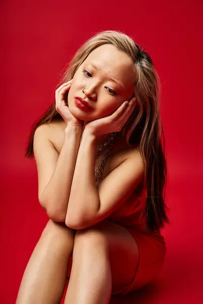 Vibrante donna asiatica in vestiti colorati seduta, mani sul viso. — Foto stock