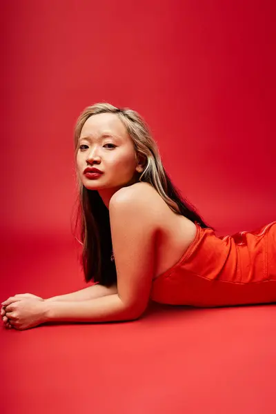 Una donna asiatica attraente in un abito rosso vibrante sdraiata con grazia a terra. — Foto stock