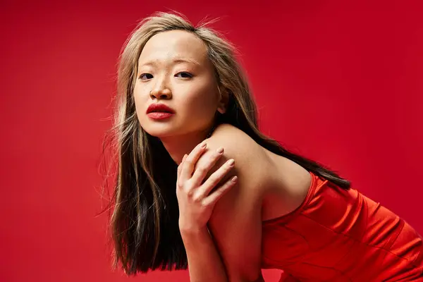 Una mujer asiática dinámica en un vestido rojo vibrante golpea una pose. - foto de stock