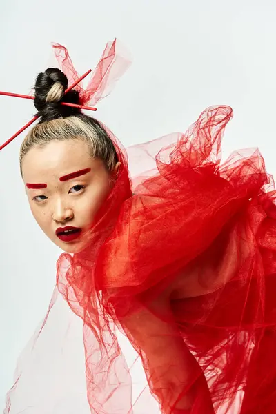 Graziosa donna asiatica in abito rosso colpisce una posa con un elegante copricapo. — Foto stock