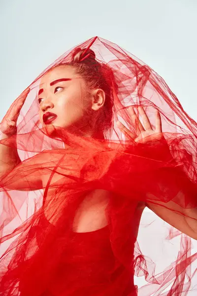 An Asian woman in a red dress poses gracefully with a veil covering her head. — Stock Photo