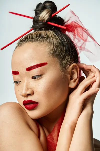Lebendige Asiatin mit rotem Make-up und Stöcken im Haar, die eine kraftvolle Pose einnimmt. — Stockfoto