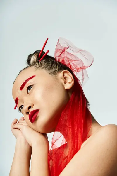 Una mujer asiática vibrante con maquillaje rojo llamativo y un velo cubierto en su cabeza posa elegantemente. - foto de stock