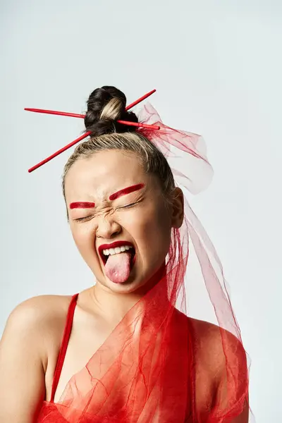 A vibrant Asian woman in a red dress cheekily sticks out her tongue. — Stock Photo