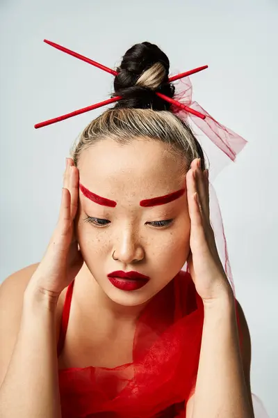 Une femme asiatique frappante ornée de maquillage rouge et de vêtements vibrants, tient dramatiquement sa tête. — Photo de stock