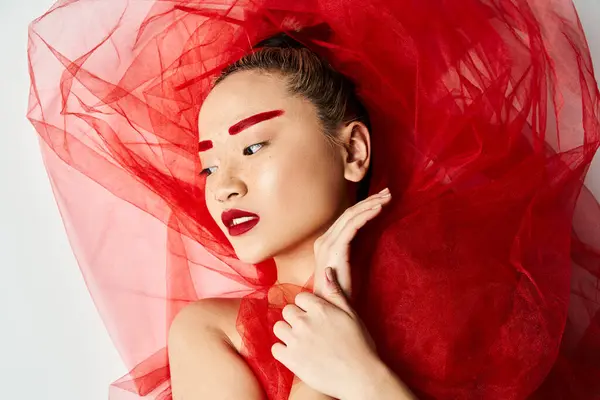 An attractive Asian woman in a vibrant red dress with a veil on her head poses gracefully. — Stock Photo