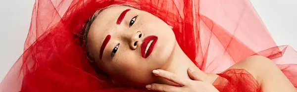A captivating Asian woman with vibrant red makeup and a flowing red veil poses gracefully. — Stock Photo