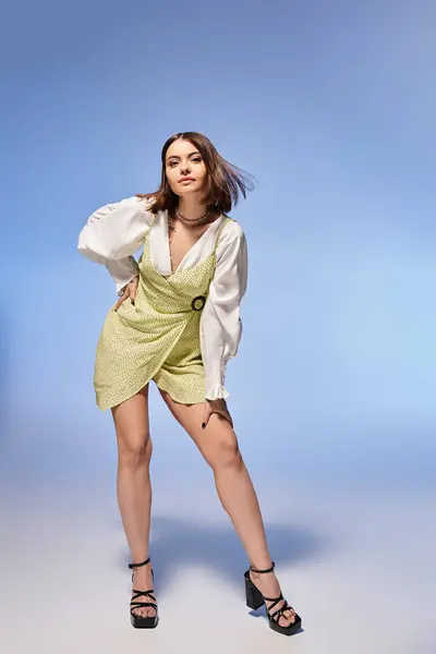 A young woman with brunette hair strikes a graceful pose in a short dress, exuding confidence and elegance in a studio setting. — Stock Photo