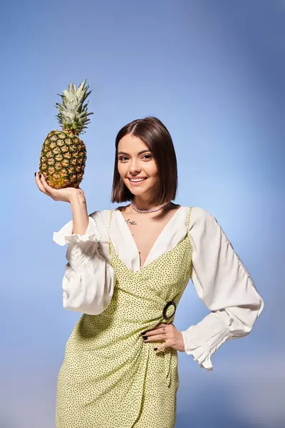 A young woman with brunette hair joyfully holds a pineapple up to her face in a studio setting. — Stock Photo