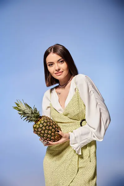 A stylish brunette woman in a dress, gracefully holding a vibrant pineapple. — Stock Photo