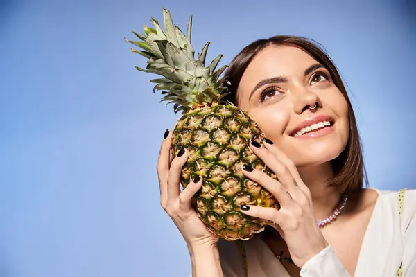 A young woman with brunette hair playfully holds a pineapple up to her face in a studio setting. — Stock Photo