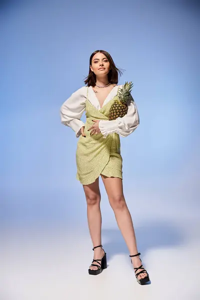Brunette woman in a graceful dress, holding a vibrant pineapple in a stylish studio setting. — Stock Photo