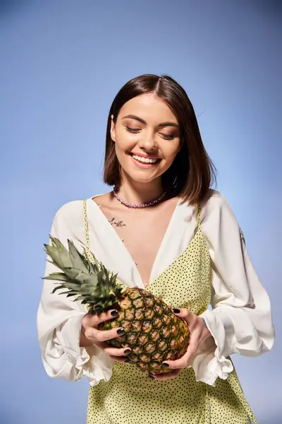 A young woman with brunette hair joyfully holds a fresh pineapple in a bright studio setting. — Stock Photo