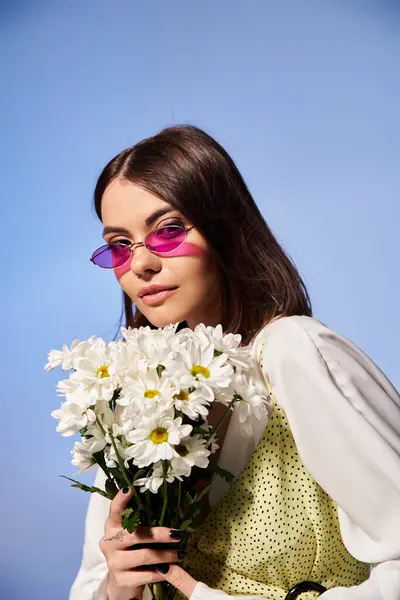 Молодая женщина с брюнетками в солнцезащитных очках держит букет маргаритки в спокойной обстановке студии. — стоковое фото