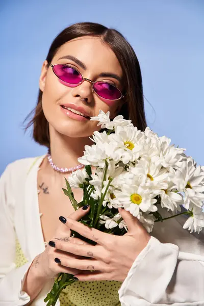Une femme brune aux lunettes de soleil tenant un bouquet de fleurs dans un décor studio. — Photo de stock